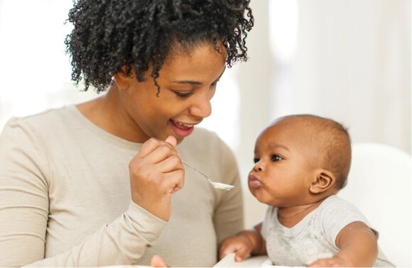 woman spoon feeding baby sitting in high chair woman spoon feeding baby sitting in high chair